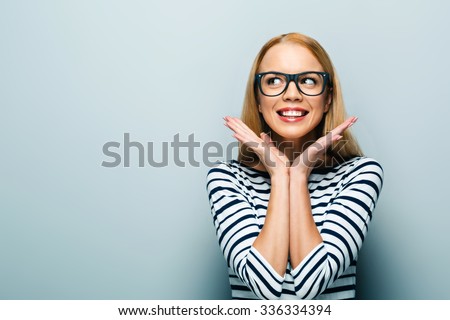 Portrait of beautiful caucasian blonde woman standing on grey background. Young woman with glasses cheerfully smiling and looking aside