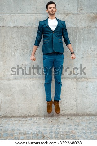 Portrait of stylish handsome young man with bristle standing outdoors near wall. Man wearing jacket and shirt. Young man jumping
