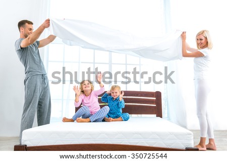 Photo of loving family of four making bed. Young family demonstrating quality of mattress and holding blanket