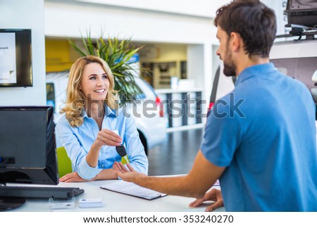 Photo of young female consultant and buyer. Young man buying new car in car showroom. Buyer receiving keys