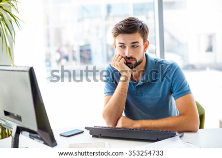 Photo of young, handsome, successful and confident businessman. Young businessman is bored while working with computer. White modern office interior