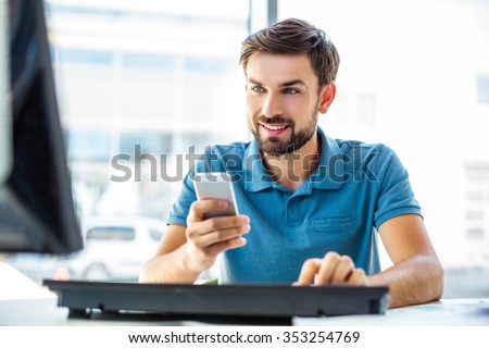 Photo of young, handsome, successful and confident businessman. Young businessman working with computer and using mobile phone. White modern office interior