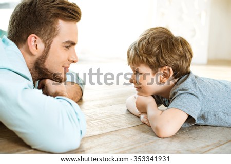 Nice family photo of little boy and his father. Boy and dad smiling and lying on wooden floor