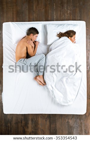 Top view photo of beautiful couple sleeping on big white bed. Young man lying on side without blanket while his girlfriend lying on side under blanket