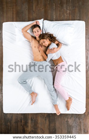 Top view photo of beautiful couple sleeping on big white bed. Young man and woman lying on back. Man hugging his girlfriend