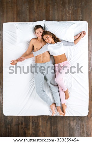 Top view photo of beautiful couple sleeping on big white bed. Young man and woman lying on back and hugging