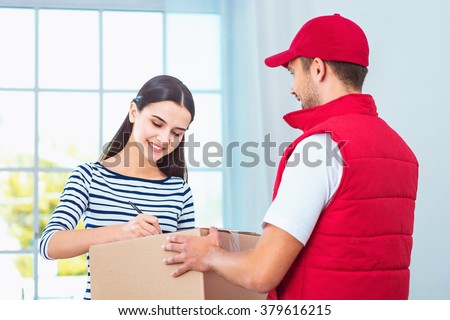 Delivery service worker in uniform delivering parcel to woman. Woman signing document on box