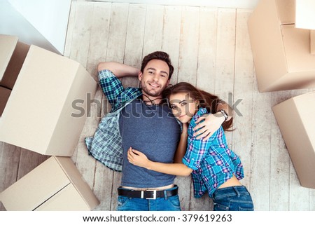 Happy young couple lying on floor near moving boxes. Young family moving to new home. Woman and man smiling and looking at camera