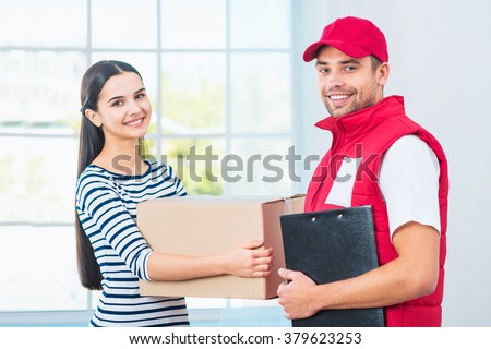 Delivery service worker in uniform delivering parcel to woman. Man with box holding document to sign and looking at camera