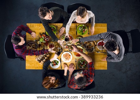 Top view creative photo of friends sitting at wooden vintage table. Friends of six having dinner. They with plates full of delicious meal and glasses with drinks. All clinking glasses