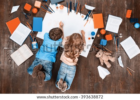 Happy children. Top view creative photo of little boy and girl on vintage brown wooden floor. Children lying near books and toys, and painting. Vintage colors