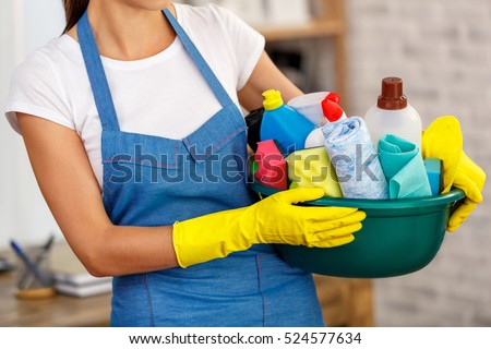Studio shot of housekeeper while cleaning office. Woman wearing gloves and holding bowl full of bottles with disinfectant