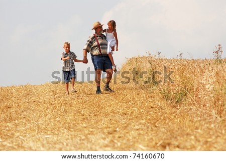 Farmer with his grandchildren walking along his wheat field