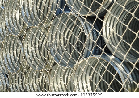 Abstract background of galvanized metal culverts behind chain link fence