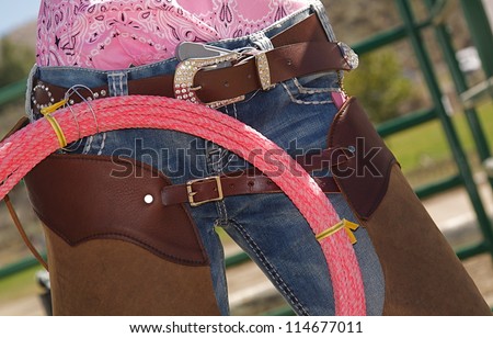 Cow girl Fashion, horseback riding apparel, rope, lasso, brown leather chaps, denim blue jeans, western belt buckle, pink blouse shirt