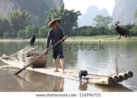YANGSHUO - JUNE 18: Chinese man fishing with cormorants birds in Yangshuo, Guangxi region, traditional fishing use trained cormorants to fish, June 18, 2012 Yangshuo in Guangxi, China