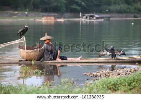Chinese man fishing with cormorants birds in Yangshuo, Guangxi region, traditional fishing use trained cormorants to fish