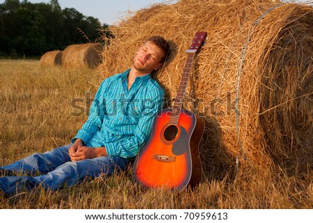The young man with a guitar has a rest in the field 	The young man with a guitar has a rest in the field