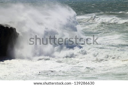 Wild sea crashing on rocks, wind forming figures in the waves. Atlantic Ocean, Cascais, Lisbon, Portugal