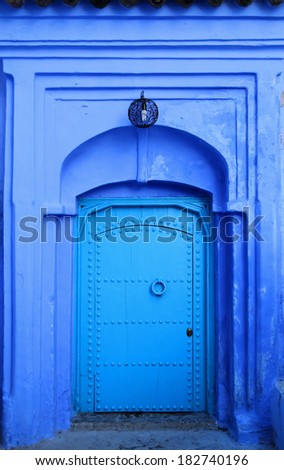 Traditional powder blue painted house facade and studded wooden door in the historical Medina of Chefchaouen, Morocco.