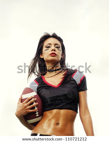 Beautiful young woman wearing American football top holding ball