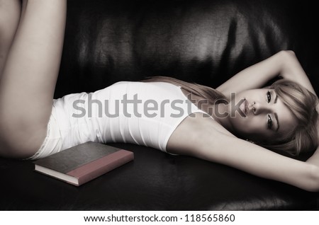 Beautiful young woman lying down on coach with book in sleep wear lingerie.