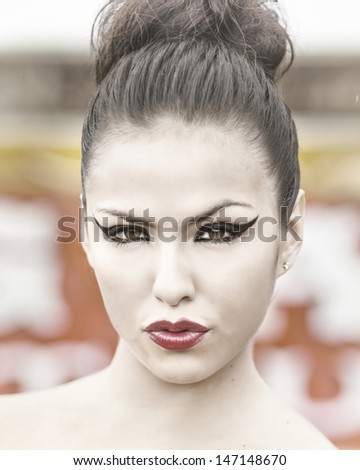 Beautiful woman pursing red lips with cat eye style liner and hair in bun.