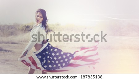 Beautiful young woman wearing denim shirt holding American flag in the open desert. Image contains scratches and noise as part of the style.