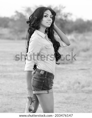 Beautiful young woman in denim shorts and top with long dark hair - desert landscape