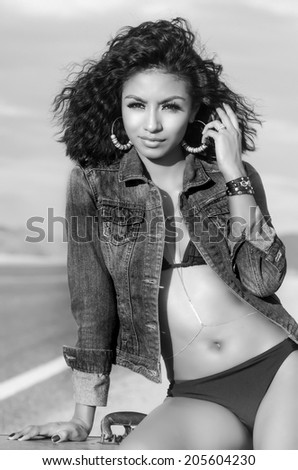 Beautiful exotic young woman wearing denim jacket and bikini on lonely desert road