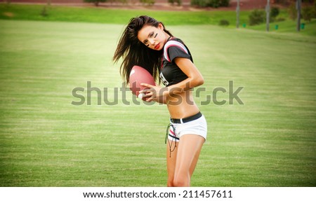 Beautiful young woman in football top and shorts holding ball ( American )