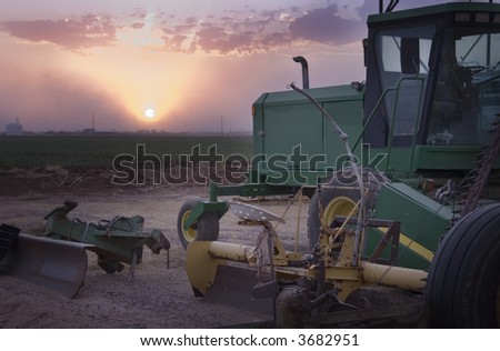 Farm machinery in foreground with silo on the horizon as the sunsets with beautiful glowing rays. a