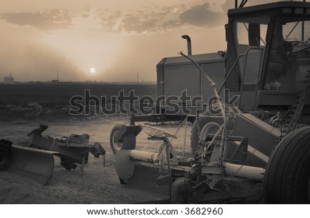 Farm machinery in foreground with silo on the horizon as the sunsets with beautiful glowing rays. a