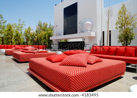 Outdoor lounge area  of nightclub and restauraunt with red chairs and cushions and a fireplace.