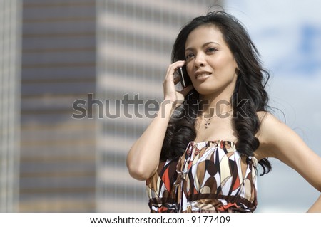 Attractive Asian American woman holding cell phone with corporate skyscraper in the background.