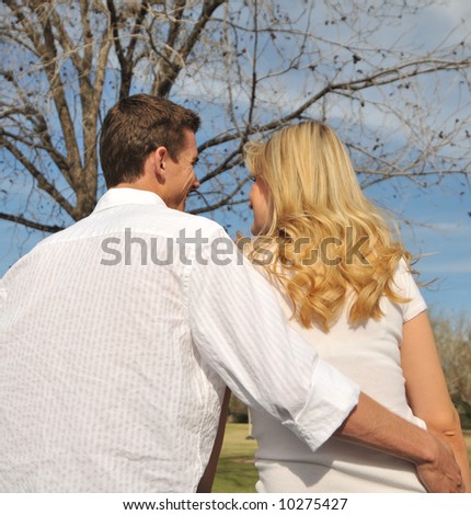 Attractive young couple sitting on a park bench with back to camera, part of an engagement shoot