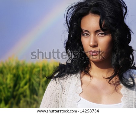 Beautiful young woman in dreamlike landscape setting with rainbow and dark silky skies.