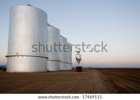 Large grain silos on farm land with sun setting.