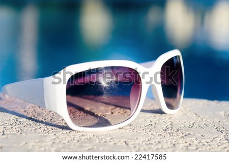 Fashionable sunglasses laying beside swimming pool