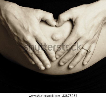 Heart shaped hands over pregnant tummy of excited  mother to be.