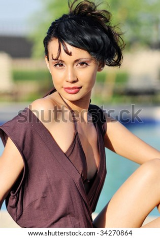 Beautiful young woman sitting beside resort club pool and patio area