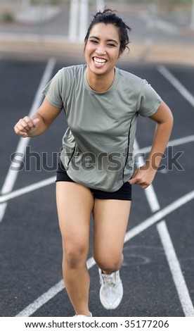 Photo of a young woman racing towards finish line with a smile on her face as she wins.  Shallow depth of field, focus on eyes, motion blue on hands and arm.