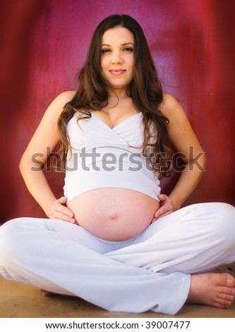 Pregnant chilled out hippie woman in yoga pose beside red background