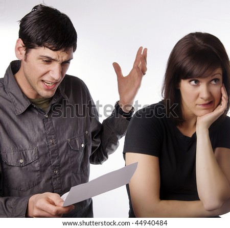 Man angry and upset after looking at credit card statement.  Wife looking embarresed.