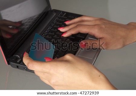 Close up of womans hands holding car and typing with other hand on laptop computer.  Woman using card while shopping online on a computer.