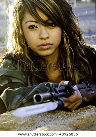 Beautiful young woman in Army Flak jacket laying on desert ground holding wire and rifle