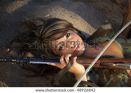 Beautiful young woman in Army Flak jacket laying on desert ground holding wire and rifle