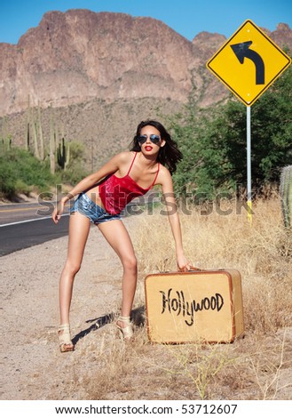 Beautiful young woman wearing red top and tiny denim shorts thumbing and hitch hiking a ride to Hollywood, California.