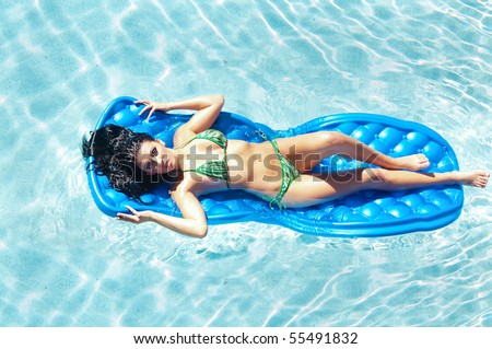 Attractive woman wearing bikini floating on foam water bed in swimming pool