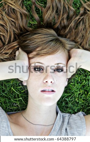 Attractive teenager woman lying down on grass looking up with beautiful hair